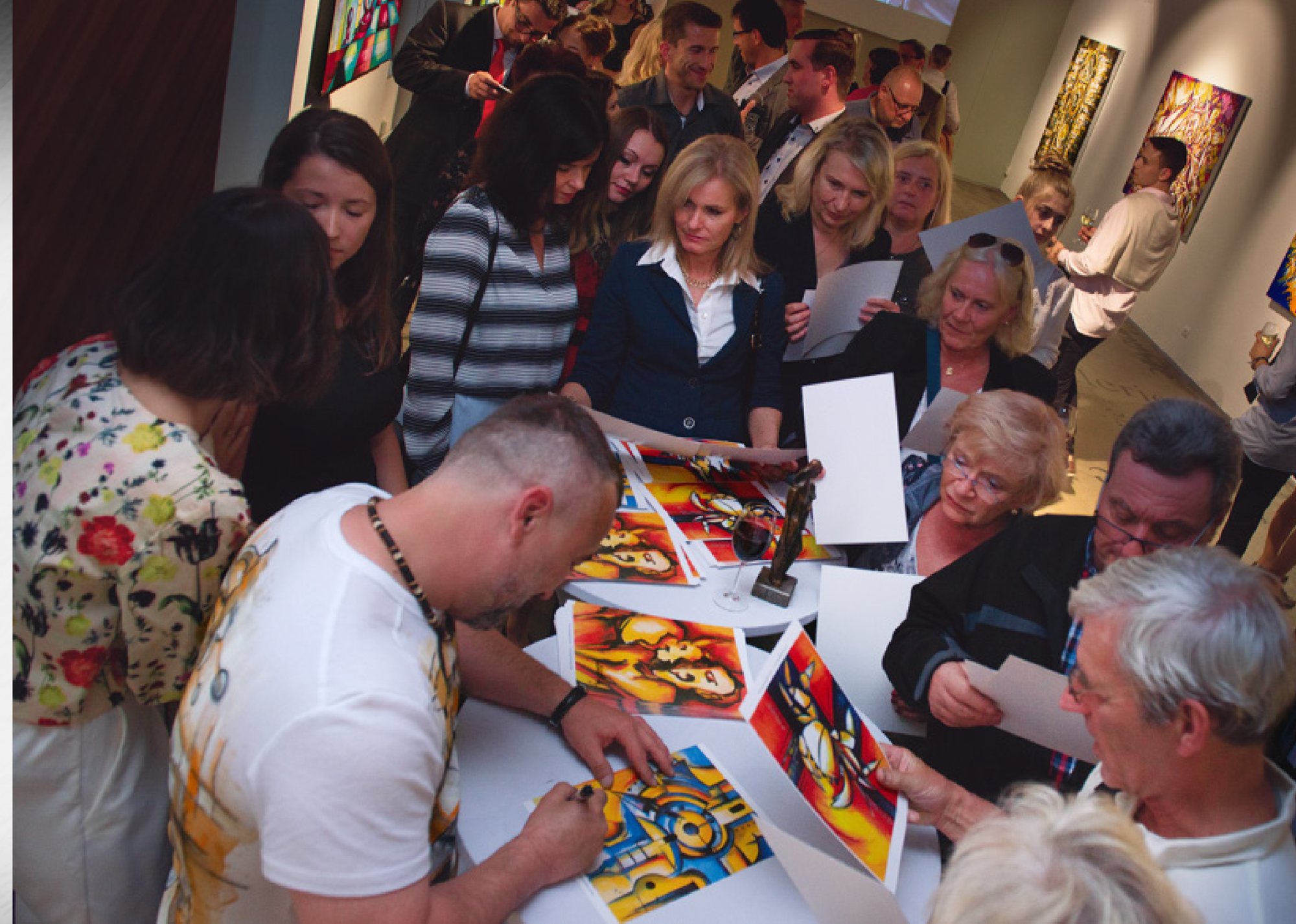 Joe Muczka jr. signing art prints surrounded by guests